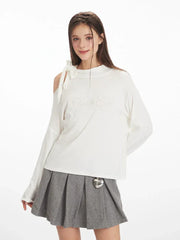 Close-up front view of a woman's upper body wearing a white long-sleeved top with one shoulder exposed and a grey pleated skirt.