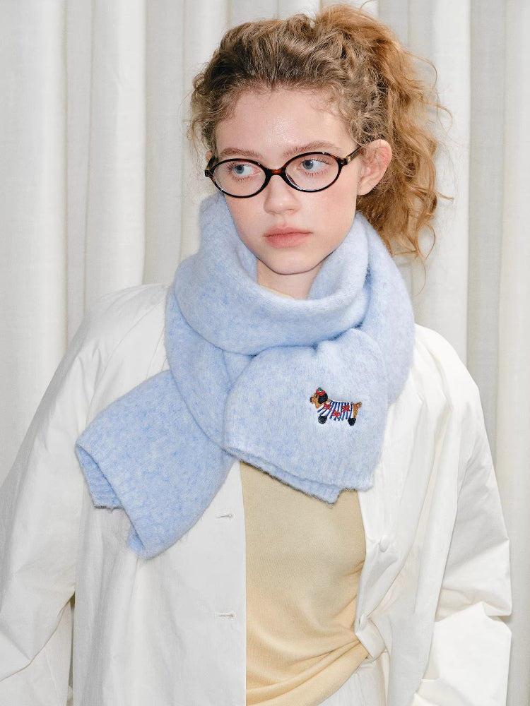 Close-up of a light blue fuzzy knit scarf with an embroidered dog detail worn by a young woman.
