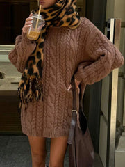 Woman wearing a brown cable knit sweater dress and a leopard print scarf, holding a drink.