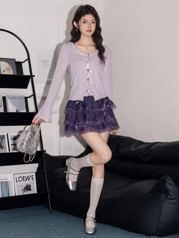 Woman posing in a lavender ribbed knit cardigan with lace trim and bow details over a white camisole, paired with a purple tiered ruffled skirt, white knee-high socks, and silver mary jane shoes.