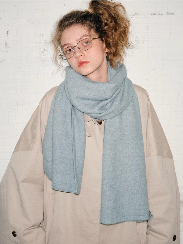 Model wearing a light beige oversized A-line coat with wide sleeves and a light blue scarf. She has on glasses and her hair is in a high ponytail.