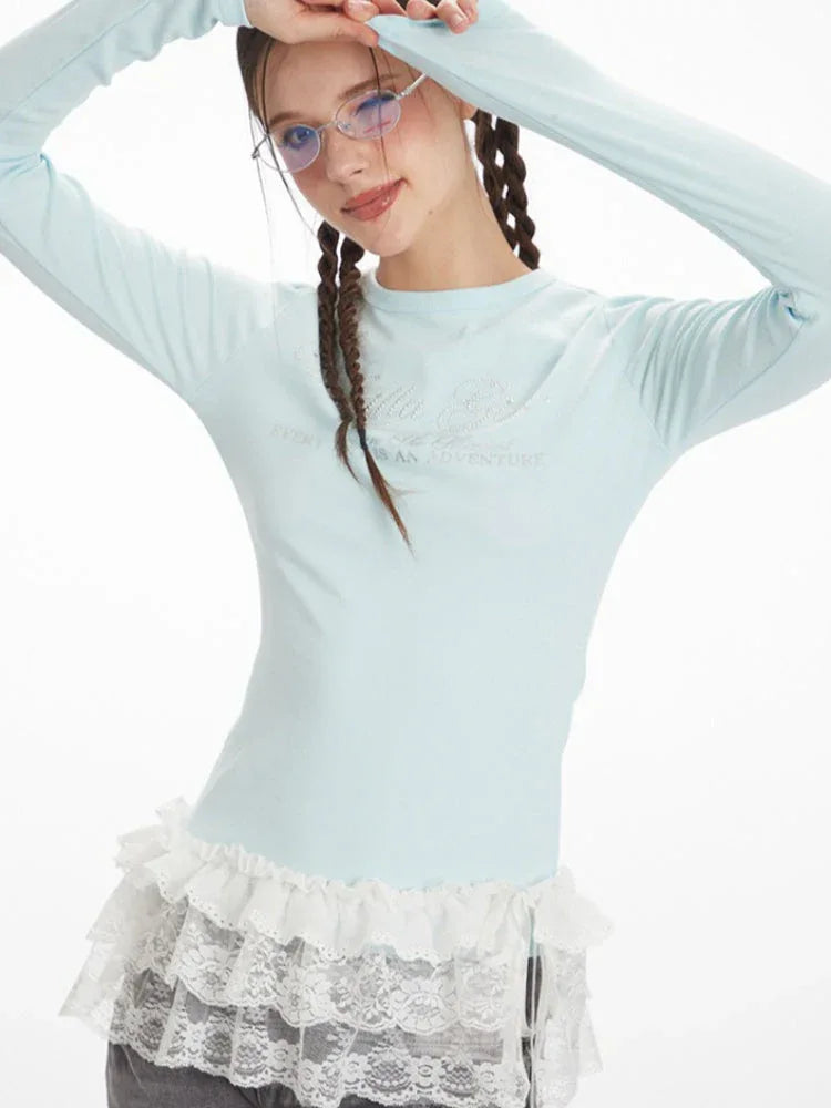 Close-up of a woman wearing a light blue long-sleeve top with white lace trim, touching her hair.