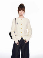Woman wearing a cream cable knit cardigan with a heart patch and dark wide-leg jeans