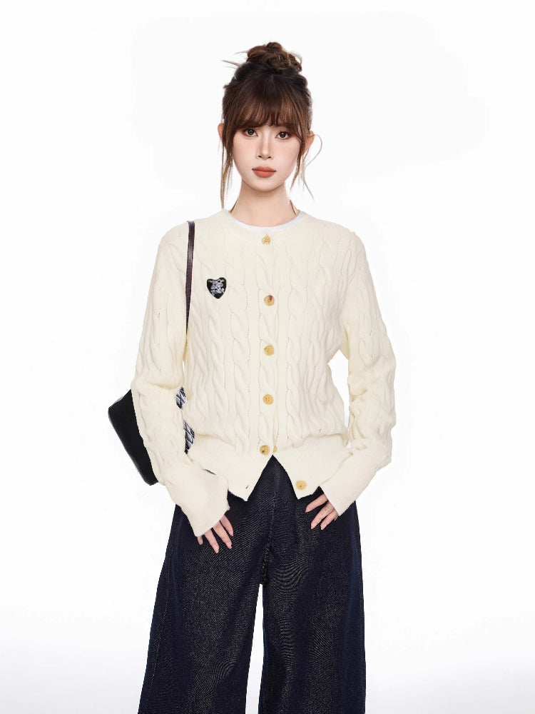 Woman wearing a cream cable knit cardigan with a heart patch and dark wide-leg jeans