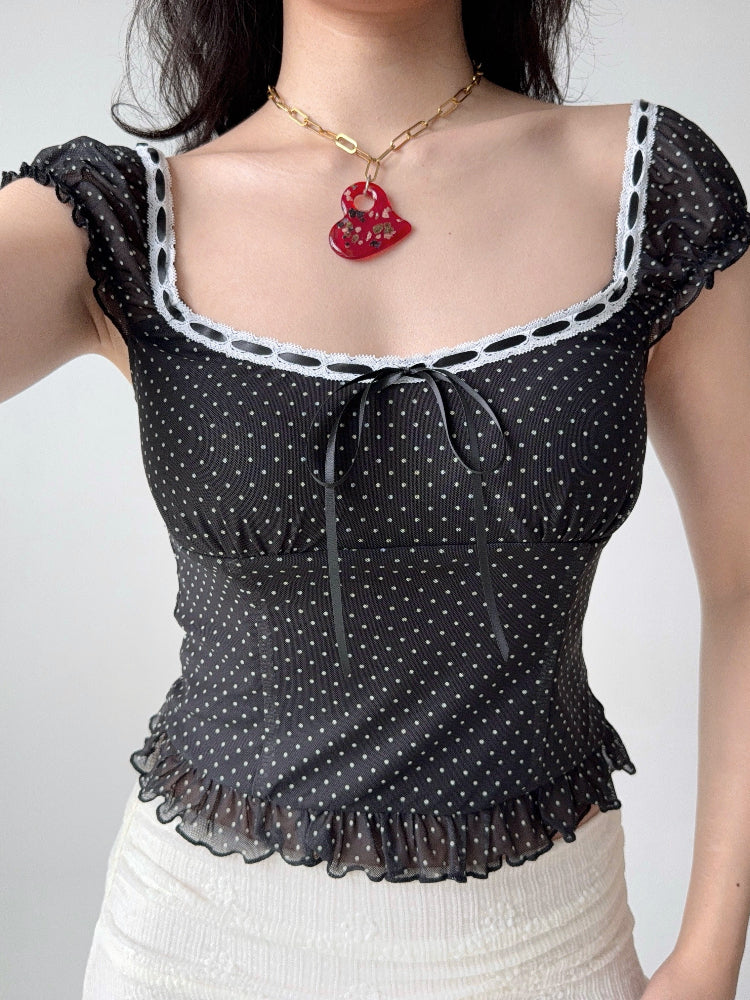 Detail shot of the neckline and tie front of a black and white polka dot mesh top.