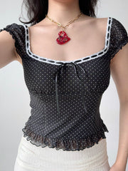 Detail shot of the neckline and tie front of a black and white polka dot mesh top.