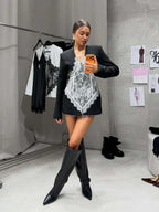 Woman wearing a black blazer with a white lace corset, knee-high black boots, and statement earrings.