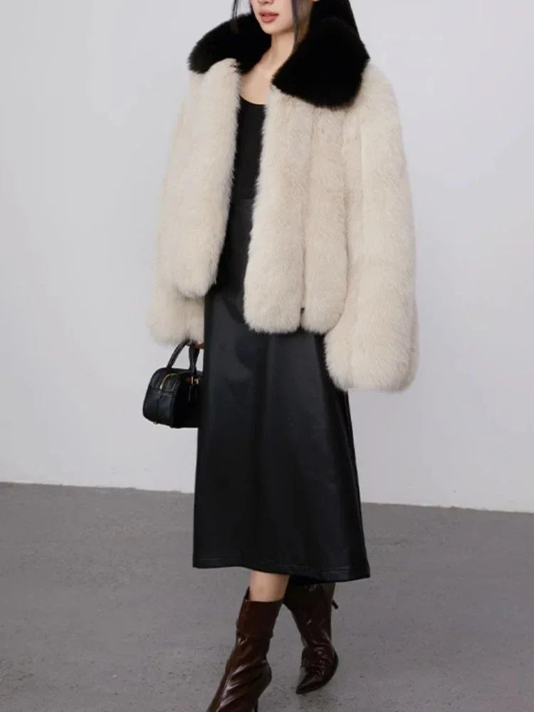 Full body shot of a woman wearing a cream faux fur cropped jacket with a black collar and a black leather dress.