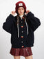 Front view of a woman wearing a dark blue hooded cardigan with colorful fruit buttons, adjusting her red beanie.