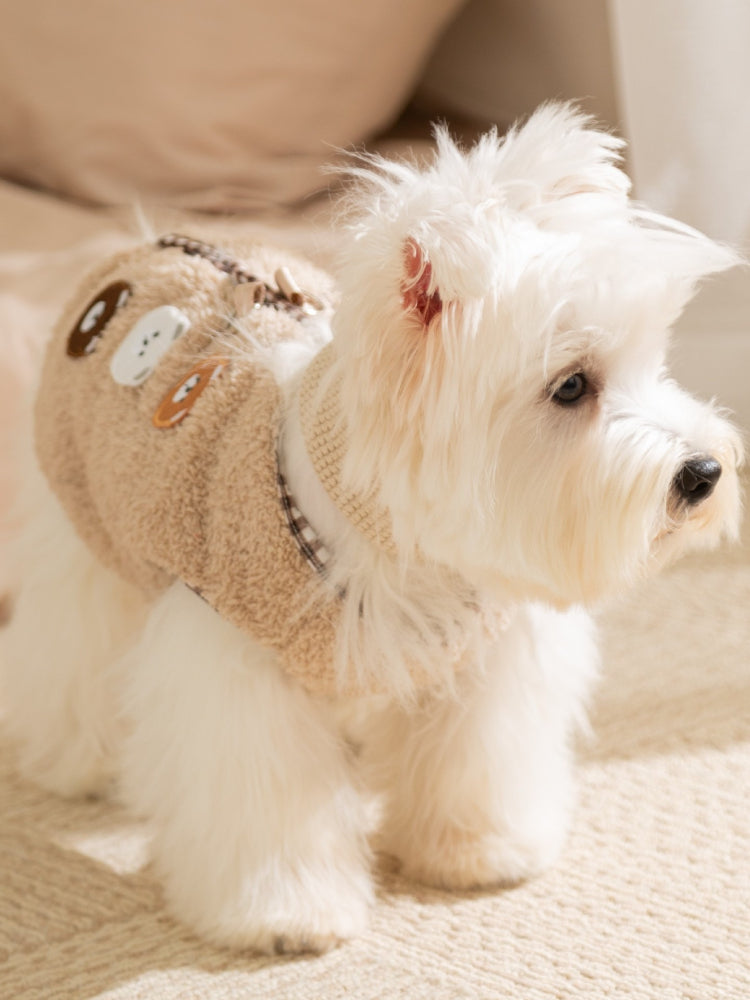 Side view of a white dog wearing a tan fleece vest with embroidered bear appliques and a checkered trim.