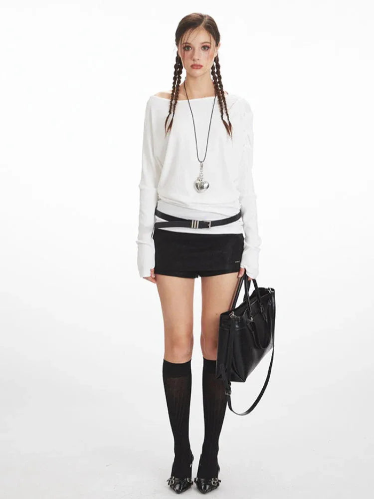 Model wearing a white off-the-shoulder long-sleeve top, black high-waisted shorts, black knee-high socks, and black heels, holding a black tote bag.