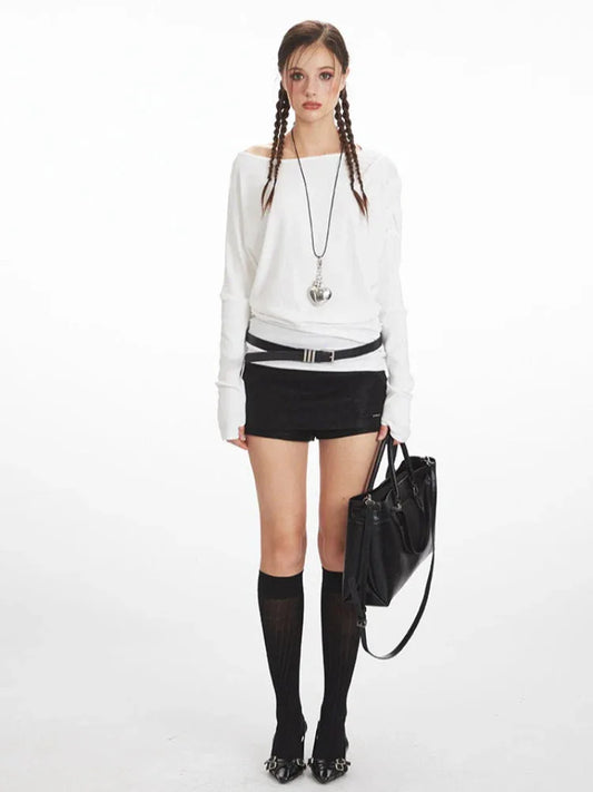 Model wearing a white off-the-shoulder long-sleeve top, black high-waisted shorts, black knee-high socks, and black heels, holding a black tote bag.