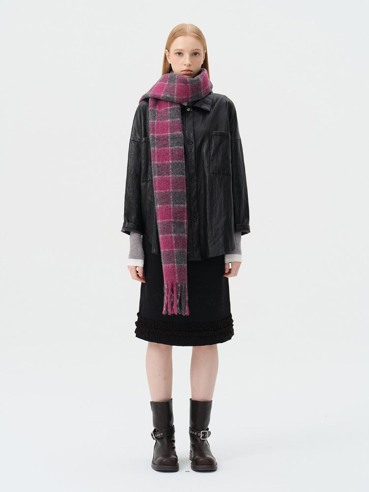 Woman wearing a black leather-look jacket, a black skirt with ruffled hem, a pink and grey plaid scarf, and black boots. Main image