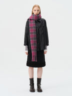 Woman wearing a black leather-look jacket, a black skirt with ruffled hem, a pink and grey plaid scarf, and black boots.