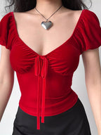 A person wearing a red velvet tie-front top with puff sleeves and a silver heart necklace.