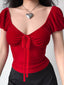 A person wearing a red velvet tie-front top with puff sleeves and a silver heart necklace.