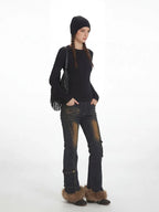 Model from the side wearing a black ribbed knit top, distressed flared jeans with fur trim cuffs, and a black beanie, with the fringe detail bag slung over the shoulder.