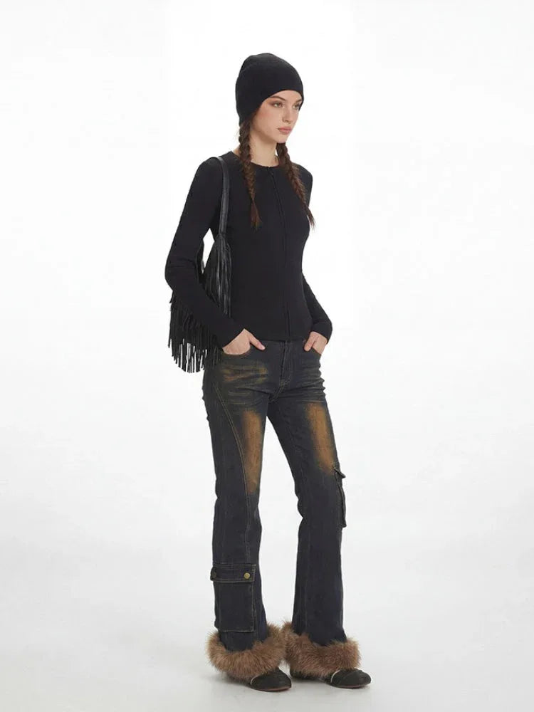 Model from the side wearing a black ribbed knit top, distressed flared jeans with fur trim cuffs, and a black beanie, with the fringe detail bag slung over the shoulder.