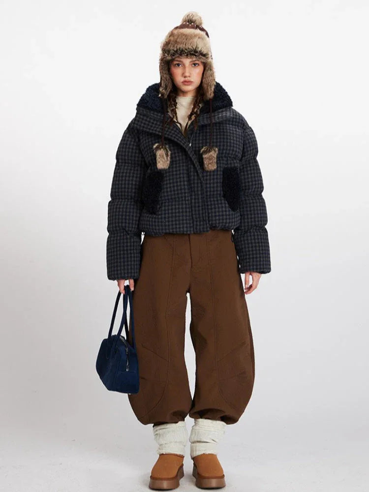 Woman wearing a plaid puffer jacket with faux fur trim and a trapper hat, holding a blue handbag. Main image