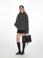 Side view of a model in a gray fuzzy bomber jacket with a plaid hem, black mini skirt, black knee-high socks, and black loafers, holding a black handbag.