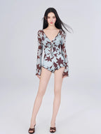 Full body shot of a woman in a floral print one-piece swimsuit with ruffled hem and long sleeves.