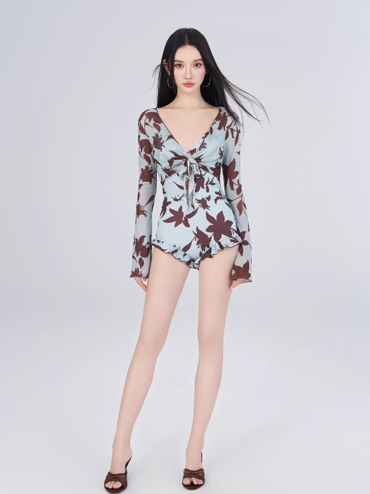 Full body shot of a woman in a floral print one-piece swimsuit with ruffled hem and long sleeves.