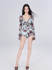Full body shot of a woman in a floral print one-piece swimsuit with ruffled hem and long sleeves.