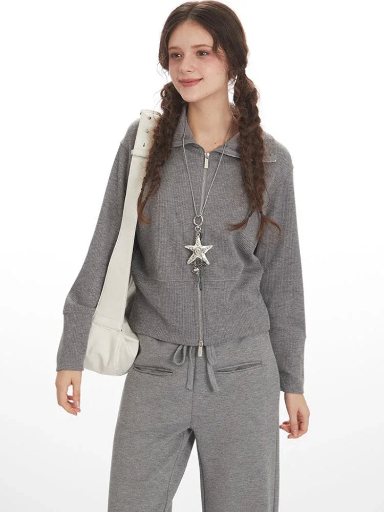 Close-up of a woman wearing a grey knit zip-up jacket and wide-leg pants, accessorized with a star pendant necklace.