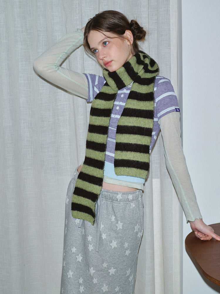 Woman wearing a striped scarf over a purple striped shirt and grey sweatpants with stars, touching her hair.