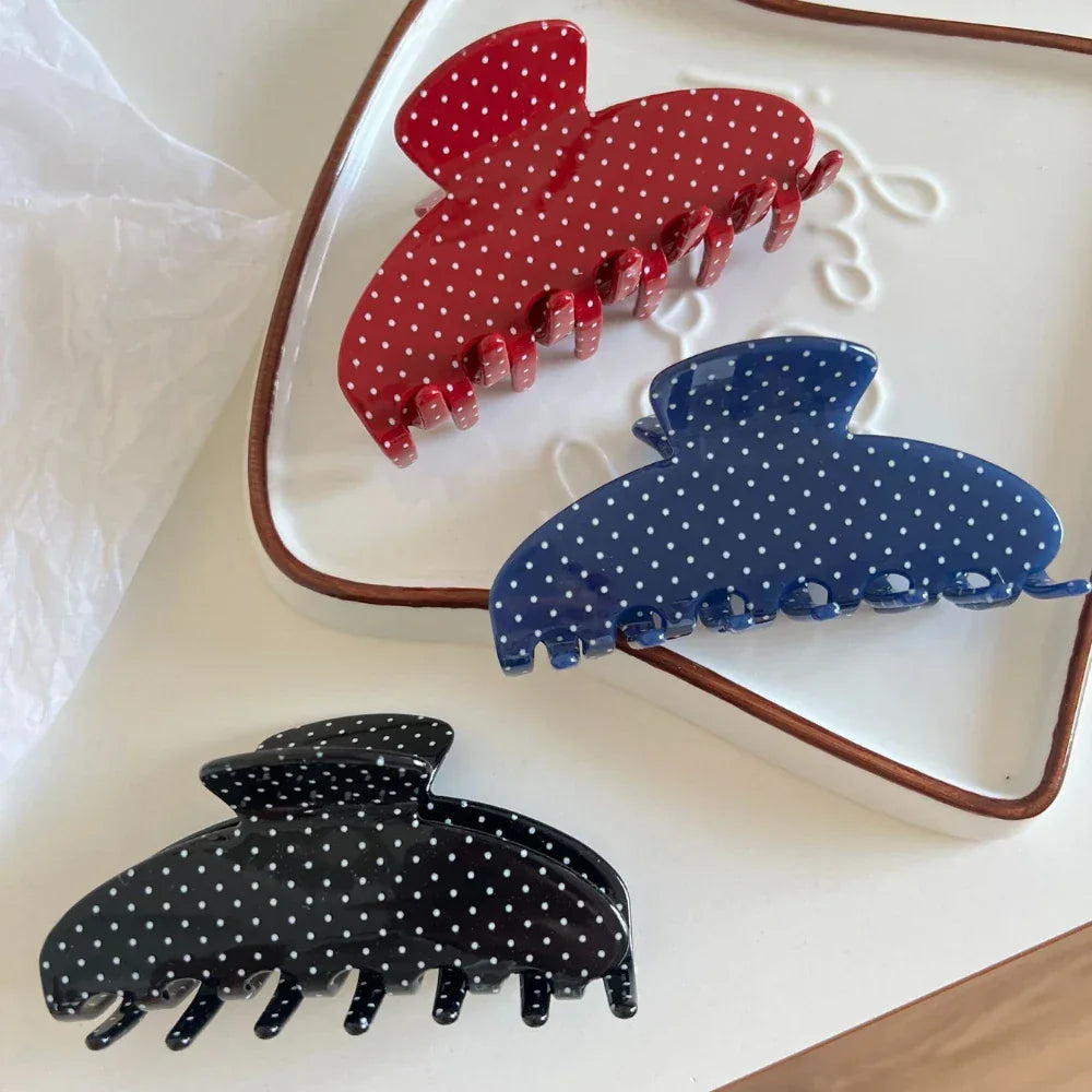 Three polka dot hair claw clips (red, blue, black) on a white tray