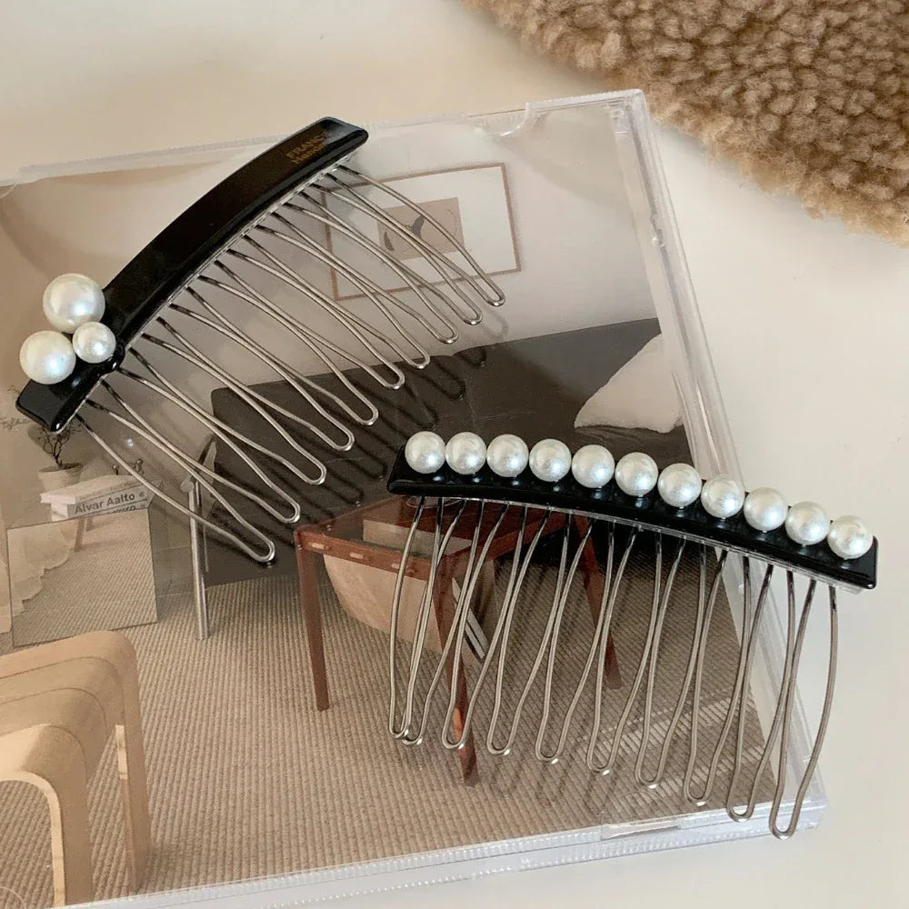Two black hair combs with pearl embellishments are placed on a clear acrylic surface, showcasing their design and the pearl details.