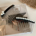 Two black hair combs with pearl embellishments are placed on a clear acrylic surface, showcasing their design and the pearl details.