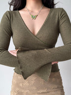 Woman crossing her arms while wearing a green ribbed wrap top with bell sleeves
