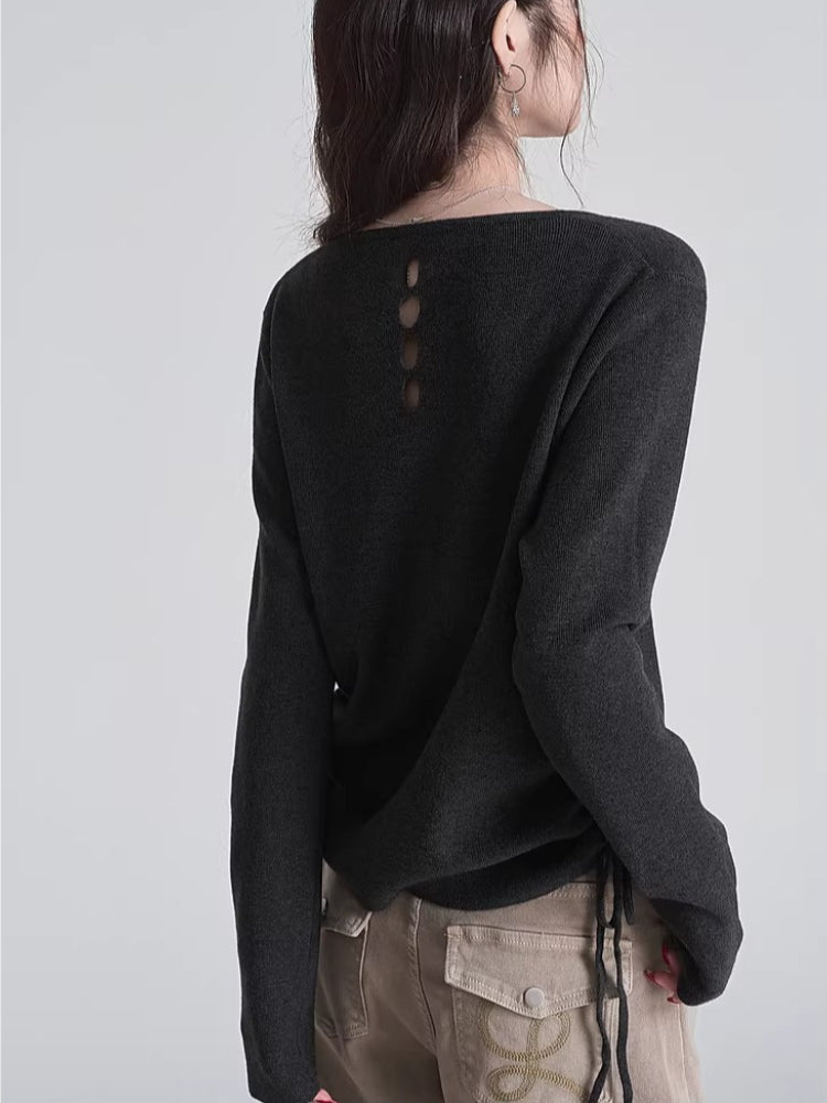 Back view of a woman wearing a dark grey knit sweater with an open detail featuring three circular cutouts.
