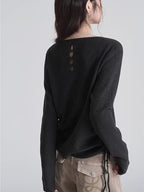 Back view of a woman wearing a dark grey knit sweater with an open detail featuring three circular cutouts.