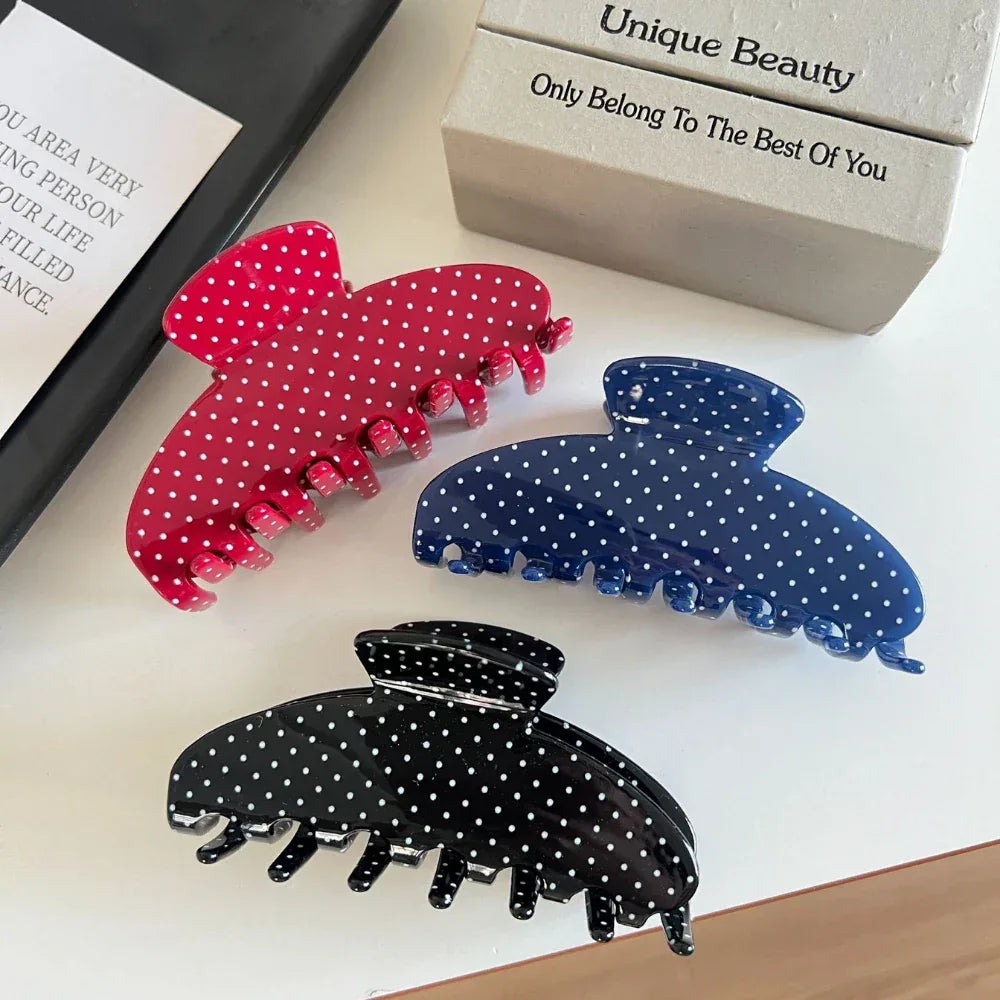 Polka dot hair claw clips in red, blue, and black arranged on a white surface with a book