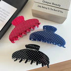 Polka dot hair claw clips in red, blue, and black arranged on a white surface with a book