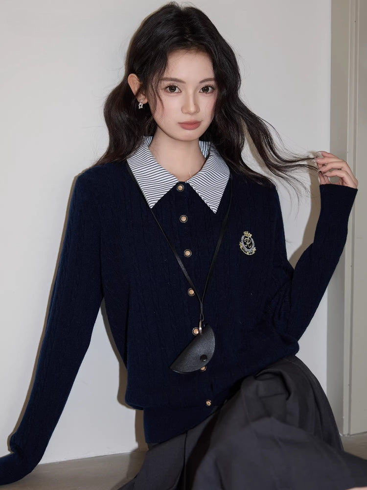 Woman with wavy dark hair wearing a navy blue cable knit cardigan with a striped collar and a gray pleated skirt.