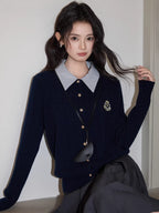 Woman with wavy dark hair wearing a navy blue cable knit cardigan with a striped collar and a gray pleated skirt.