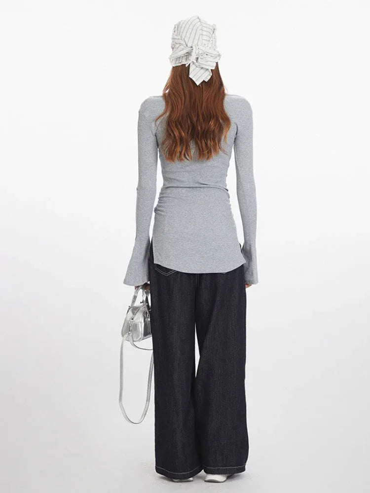 Back view of a woman wearing a grey long-sleeve ribbed knit top with bell sleeves and dark wash wide-leg jeans, holding a silver handbag.