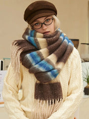 Model wearing a cream cable knit sweater and a brown plaid scarf with cream, blue, and brown stripes. She is also wearing a brown flat cap and round glasses.