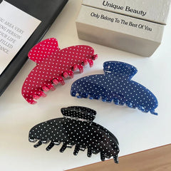 Polka dot hair claw clips in red, blue, and black arranged on a white surface with a book
