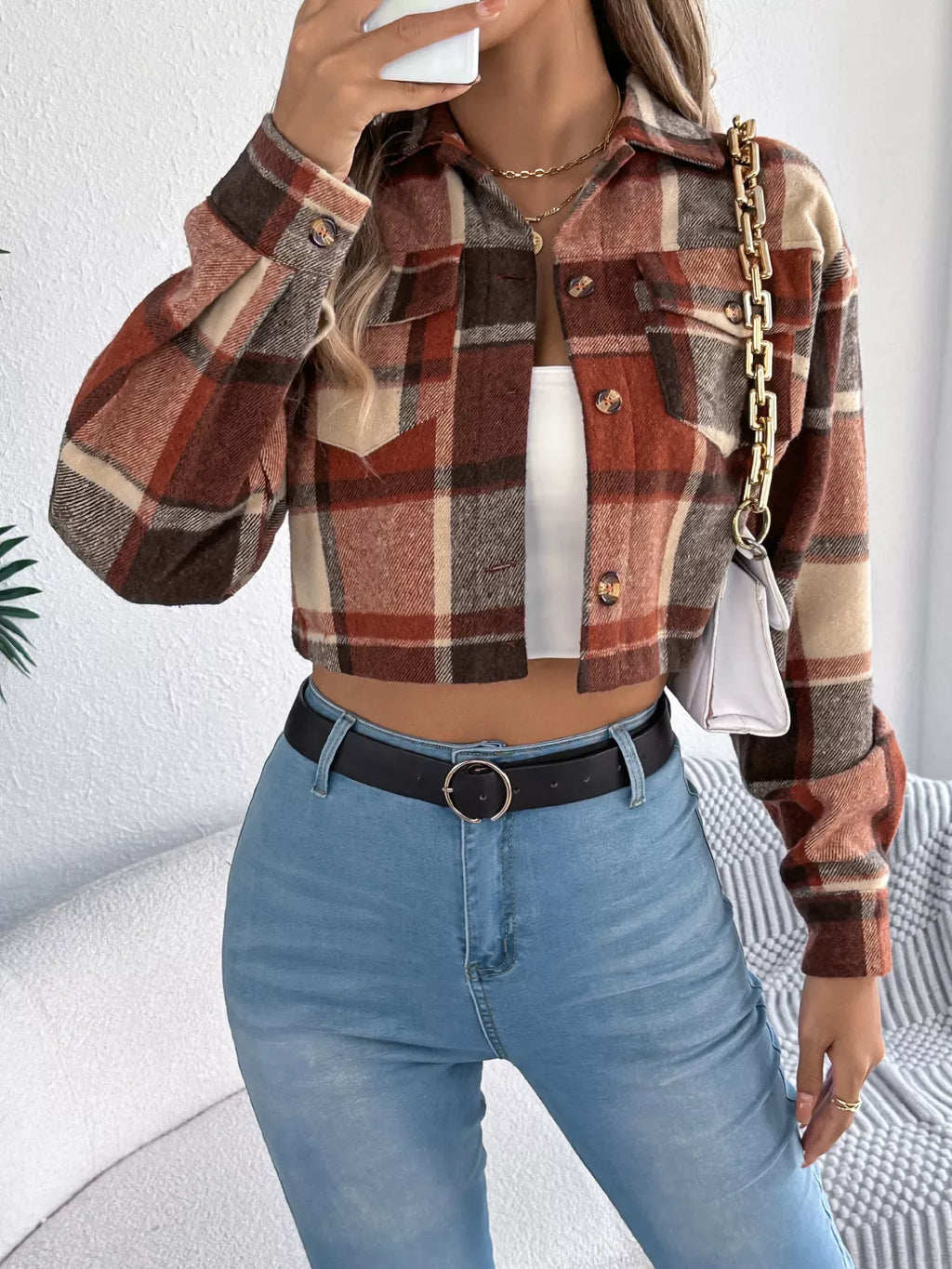 Model holding a white quilted handbag while wearing a cropped plaid jacket, white tank top, and blue jeans.