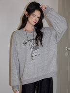Woman posing with a grey crew neck sweatshirt with a graphic print