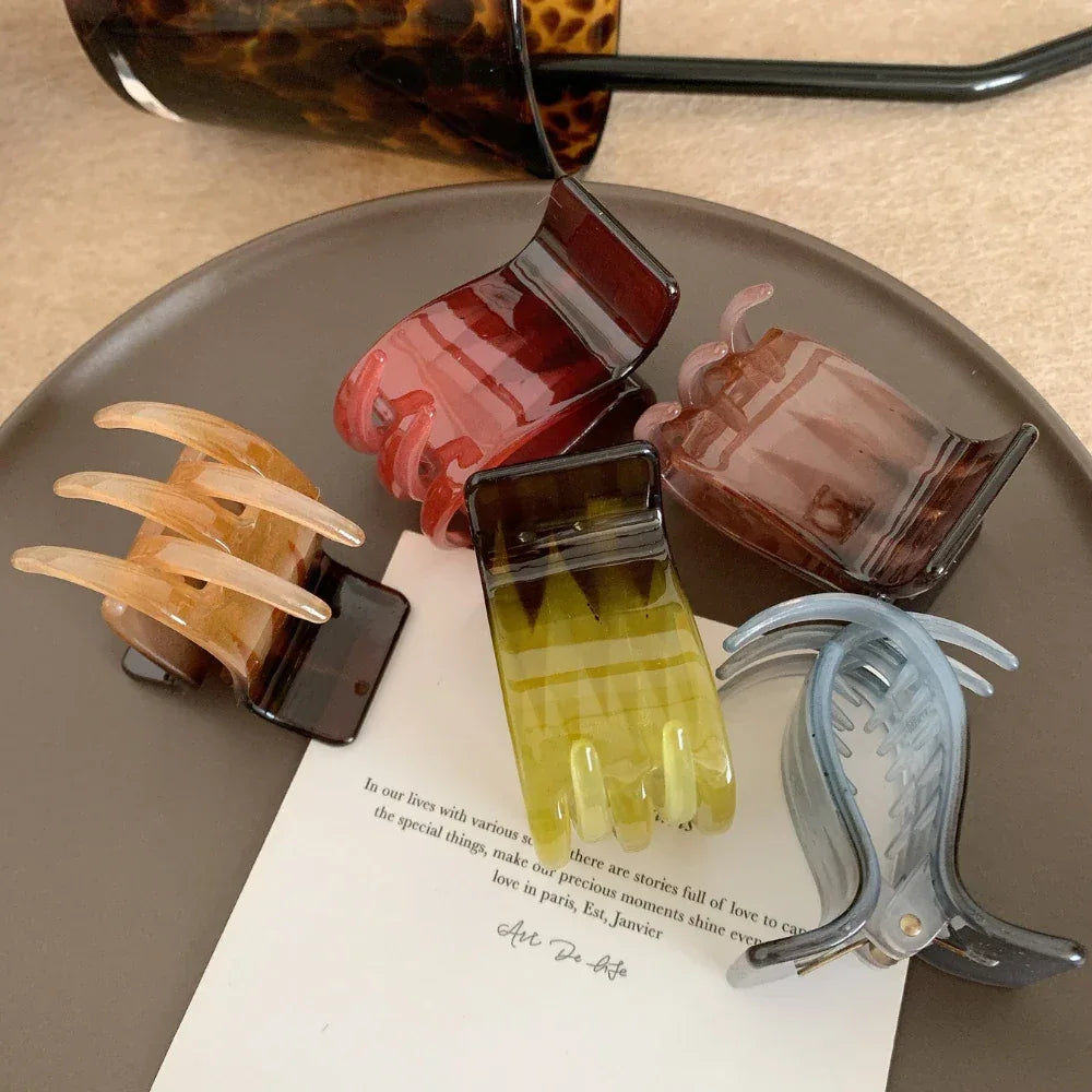 A collection of five hand-shaped claw clips in various colors including red, pinkish-brown, green, and brown, arranged on a brown plate.