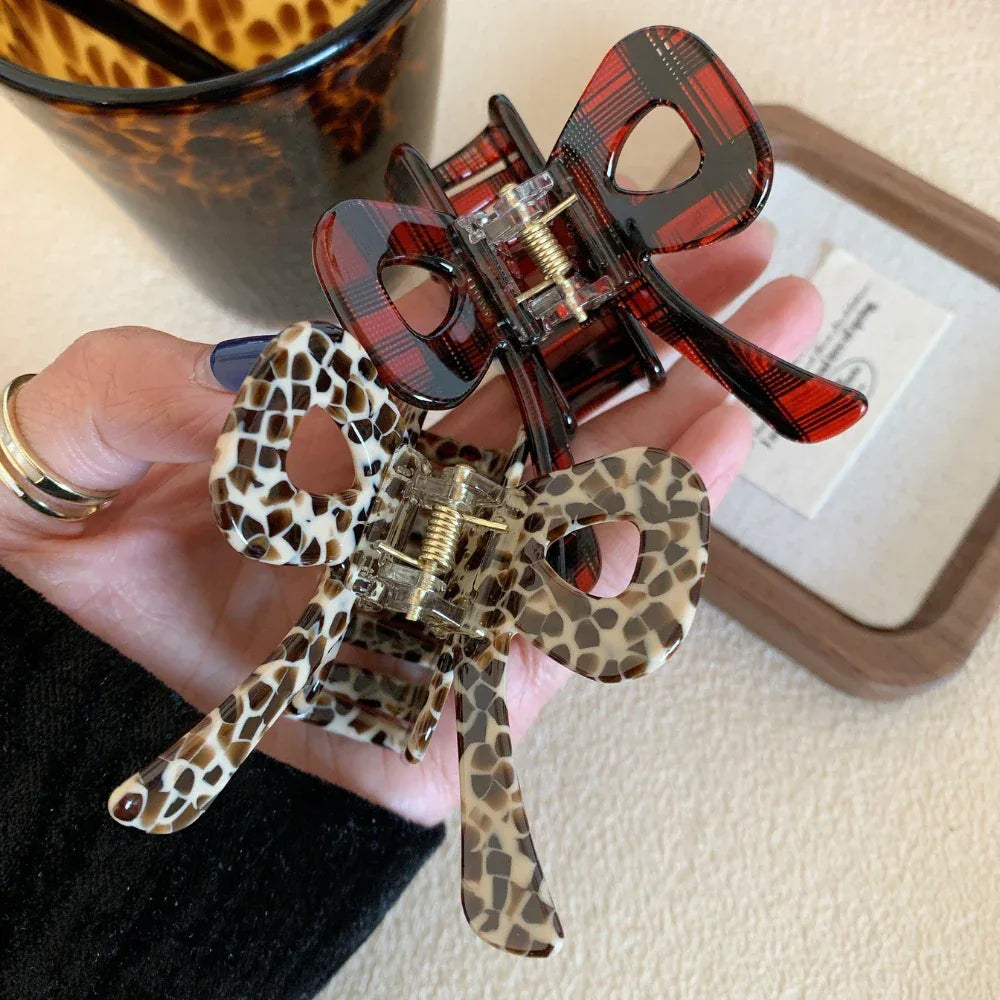Two bow hair clips, one with a leopard print and one with a tortoiseshell pattern, held in a hand