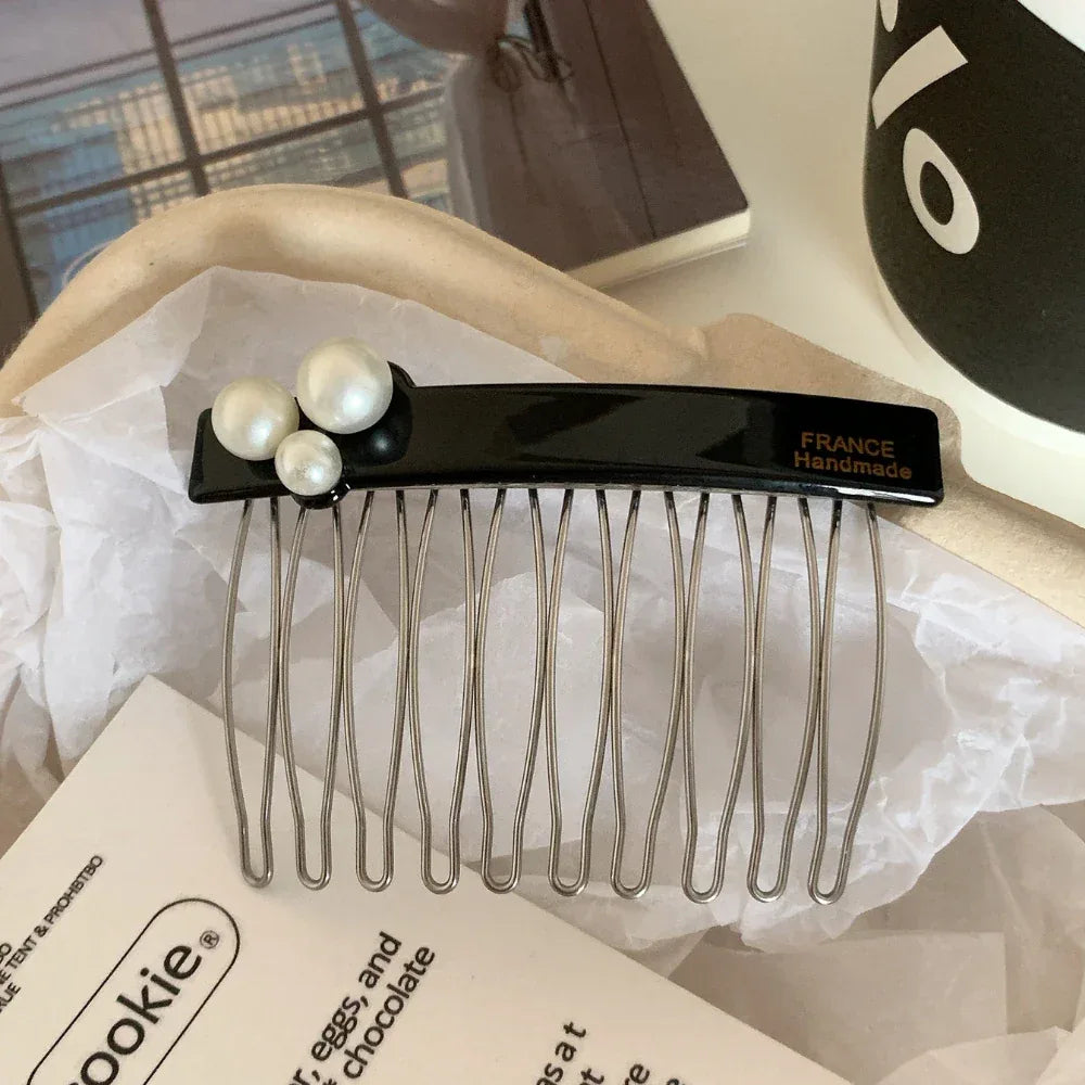 A black hair comb with three white pearls and the "FRANCE Handmade" inscription is presented in a box with white paper and a booklet.