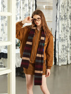 Woman in a brown bomber jacket and mini skirt, wearing glasses and a striped scarf.
