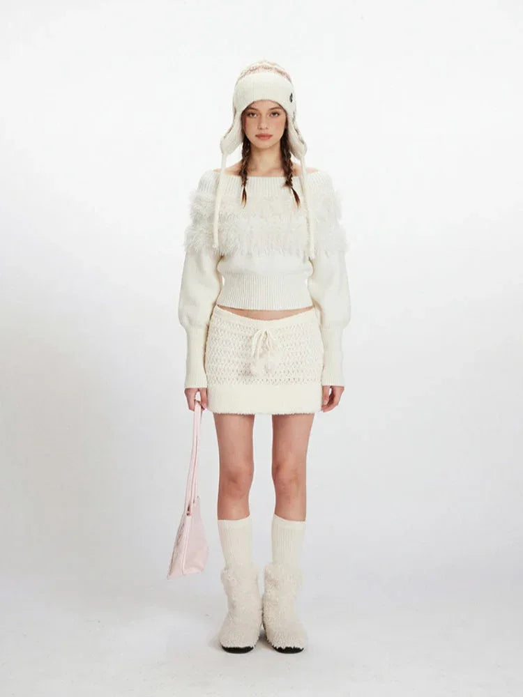 Model wearing a white off-the-shoulder sweater and matching mini skirt with a white knit hat, white knee-high socks, and white fuzzy boots. She is holding a pink handbag.