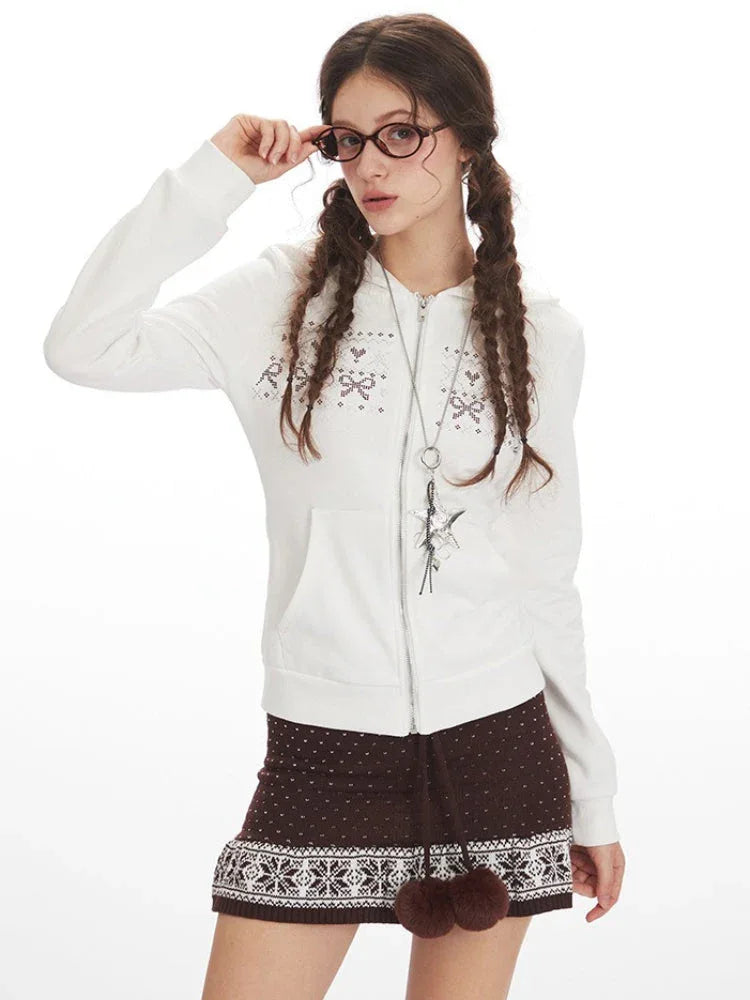Close-up of a woman wearing a white zip-up hoodie with a decorative pattern, adjusting her glasses.